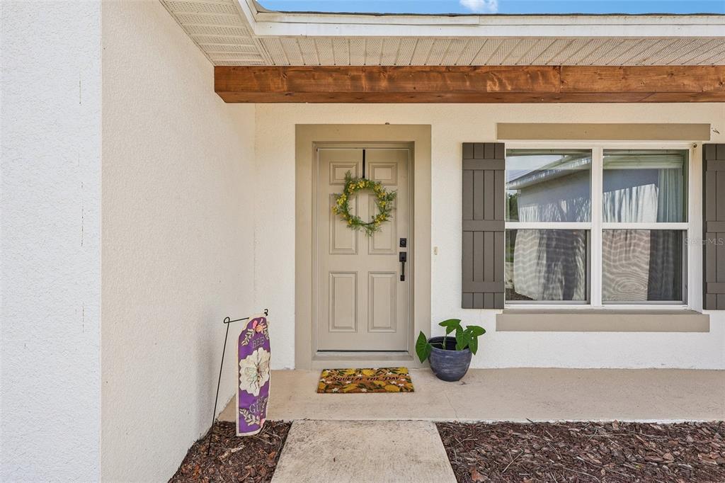 The exterior front entrance features a beige door, a wreath, and a small garden flag — 12020 VIRGINIA DRIVE, LEESBURG, FL