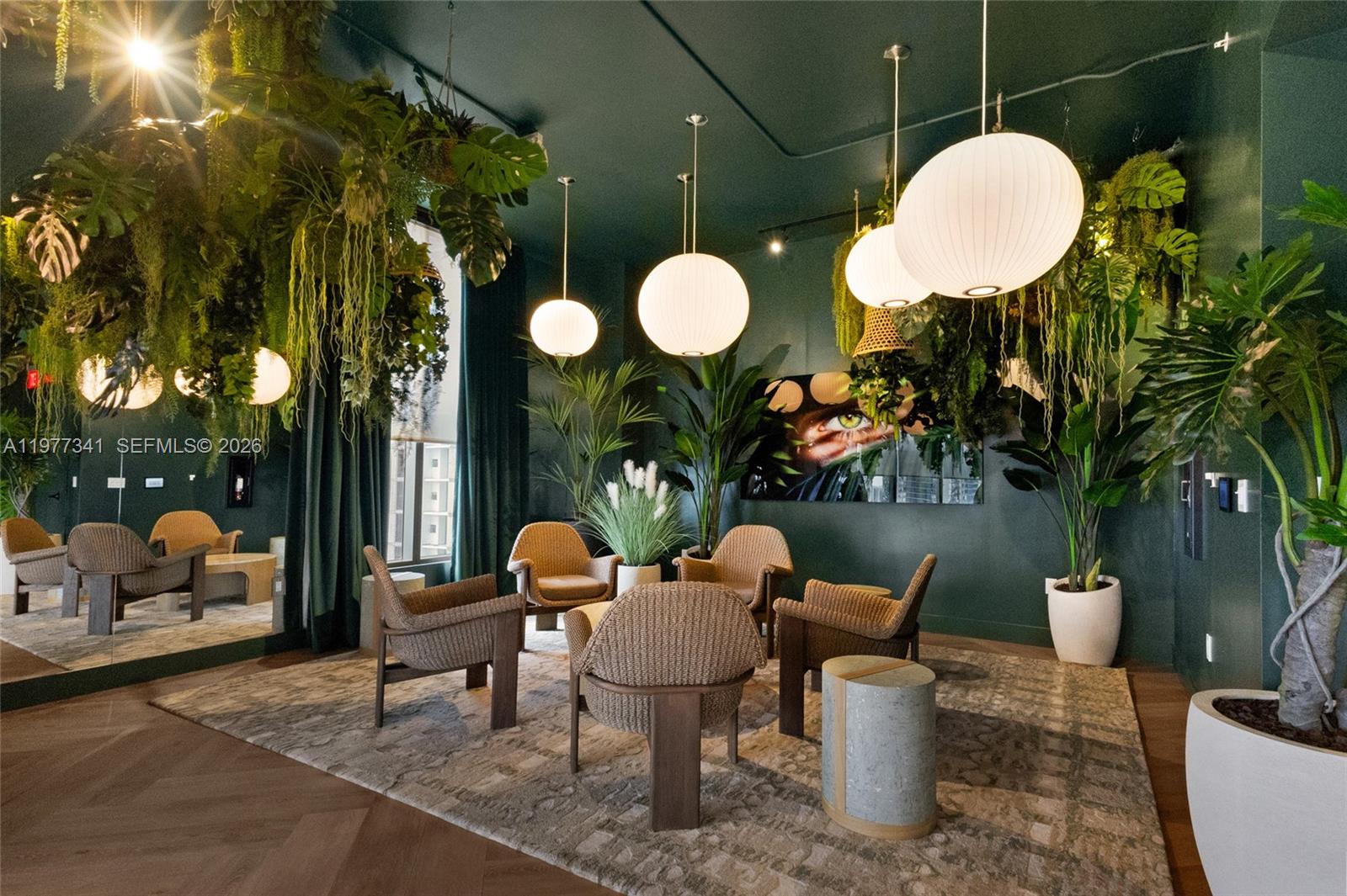 A lounge area features dark green walls, hanging plants, globe pendant lights, and wicker chairs — 121 NE 5 ST # 1500, Miami FL 33132, MIAMI, FL