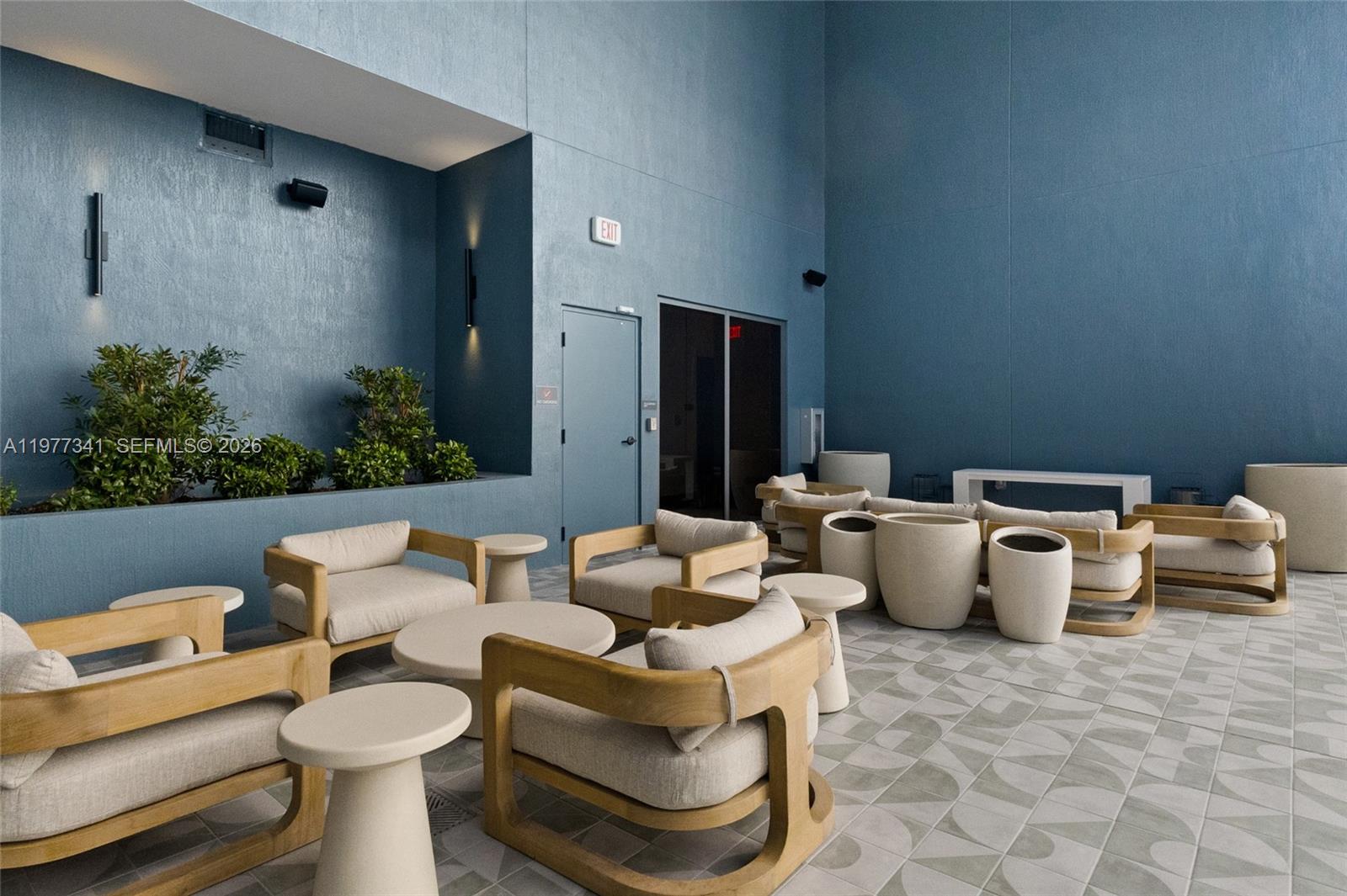 An outdoor lounge area features blue walls, light-colored wooden armchairs, and patterned tile flooring — 121 NE 5 ST # 1500, Miami FL 33132, MIAMI, FL