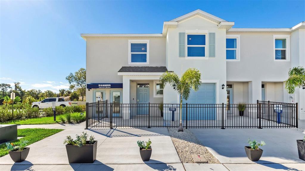A two-story townhouse exterior features a light-colored facade, a blue garage door, and metal fencing — 4036 GOLD DUST LANE, SARASOTA, FL