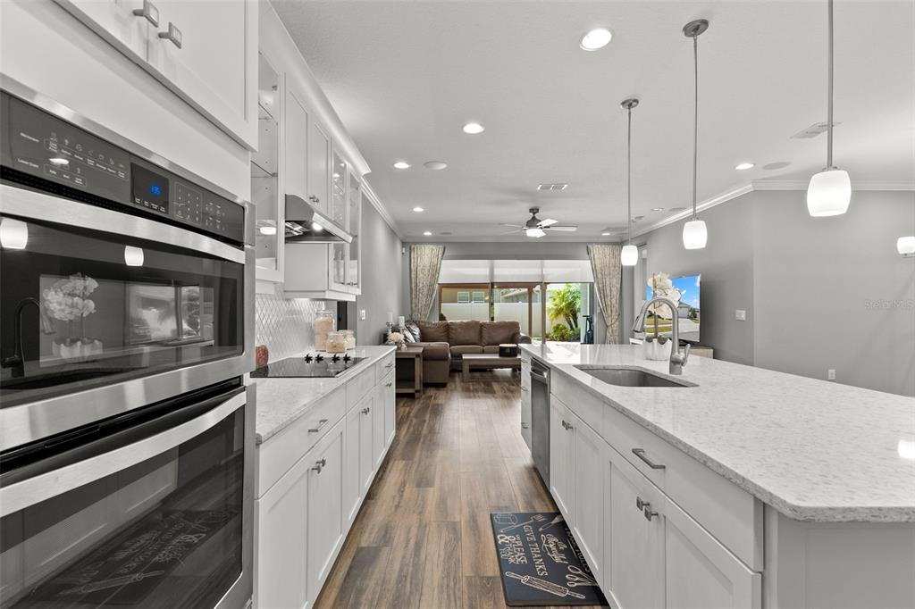 A modern kitchen with white cabinets and quartz countertops opens into a living room area — 12109 NIGHT JASMINE COVE, RIVERVIEW, FL