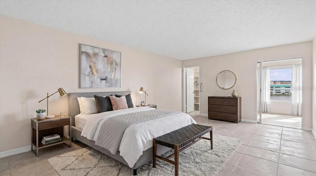 A bedroom features a gray upholstered bed, a wooden bench, and a sliding door to a balcony — 5925 SHORE BOULEVARD S UNIT 302, GULFPORT, FL