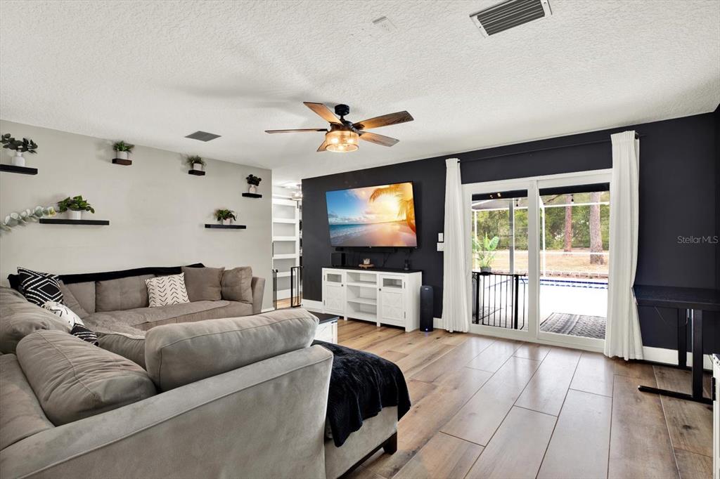 A living room features a grey sectional sofa, a dark accent wall, and sliding glass doors — 4118 RAMONA DRIVE, SPRING HILL, FL