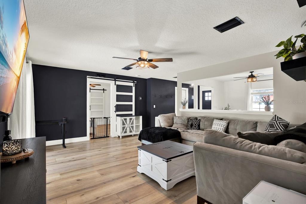 A living room features dark accent walls, light wood-look flooring, and a large sectional sofa — 4118 RAMONA DRIVE, SPRING HILL, FL