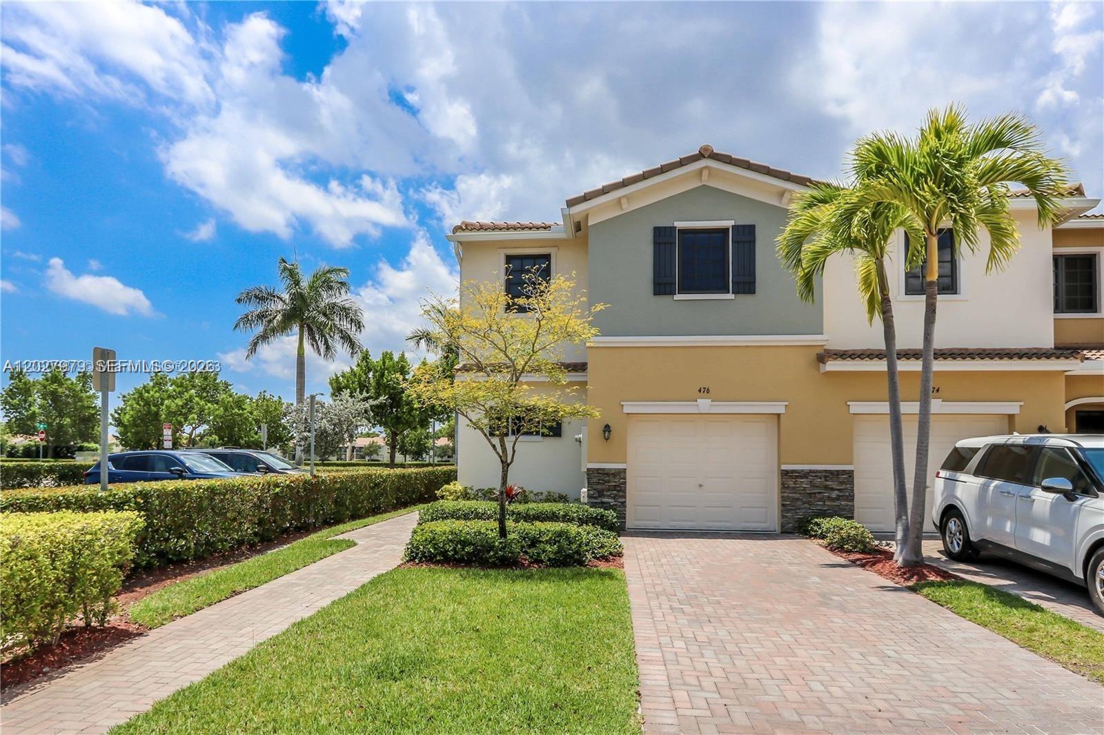 A two-story townhouse with a paved driveway, a single-car garage, and palm trees — 476 NE 194th Ter, Miami FL 33179, MIAMI, FL