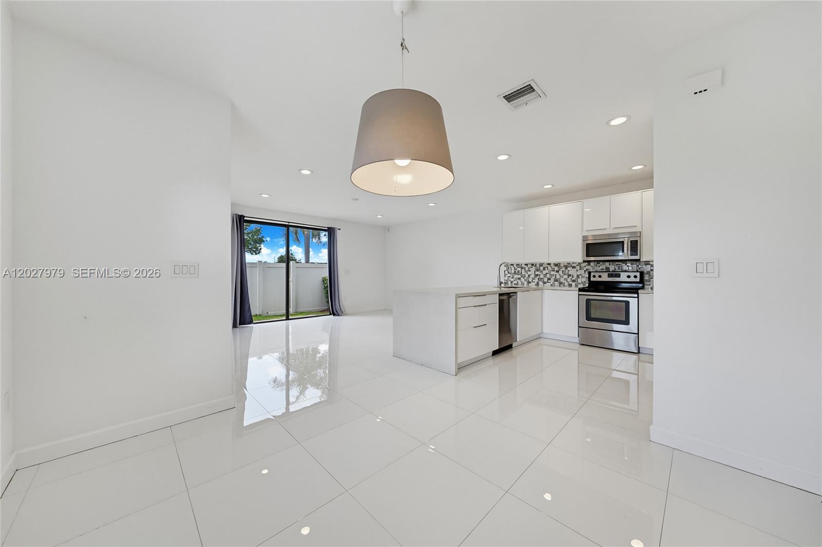 A modern kitchen and dining area feature white cabinetry, stainless steel appliances, and glossy tile floors — 476 NE 194th Ter, Miami FL 33179, MIAMI, FL