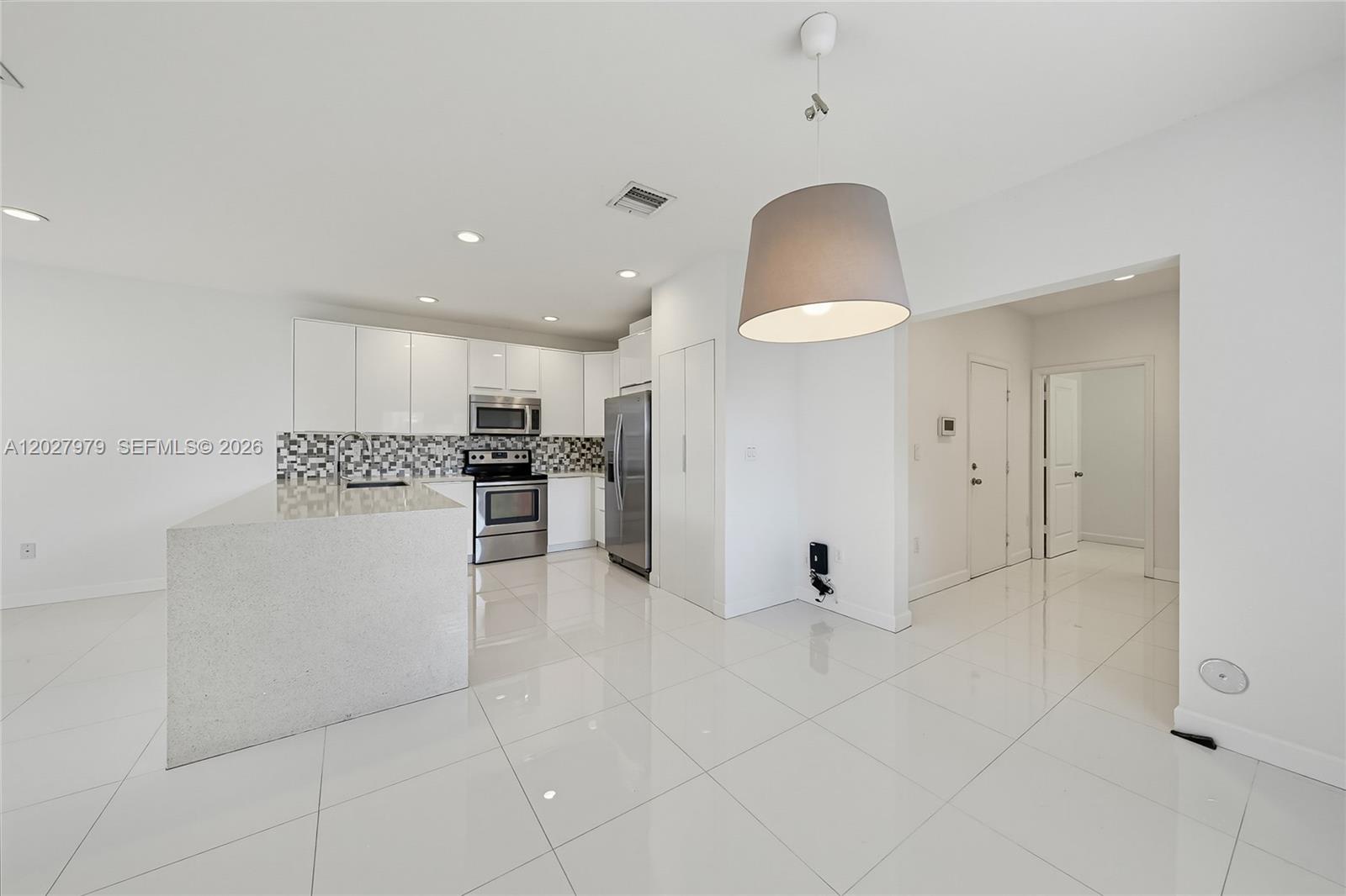A modern kitchen features white cabinetry, stainless steel appliances, a stone island, and tiled floors — 476 NE 194th Ter, Miami FL 33179, MIAMI, FL