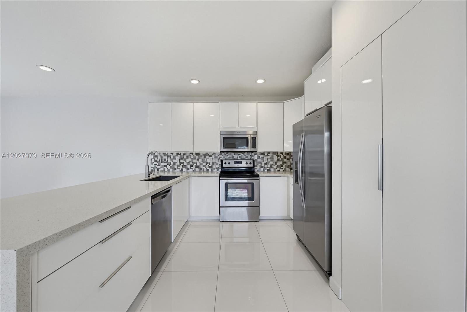 A modern kitchen features white flat-panel cabinets, stainless steel appliances, and a tiled backsplash — 476 NE 194th Ter, Miami FL 33179, MIAMI, FL