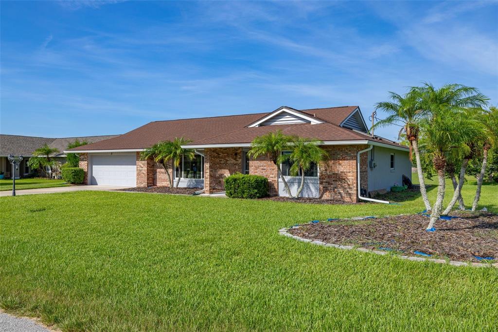 A single-story brick house with a brown shingled roof, two-car garage, and palm trees — 2 CLAYMONT COURT S, PALM COAST, FL