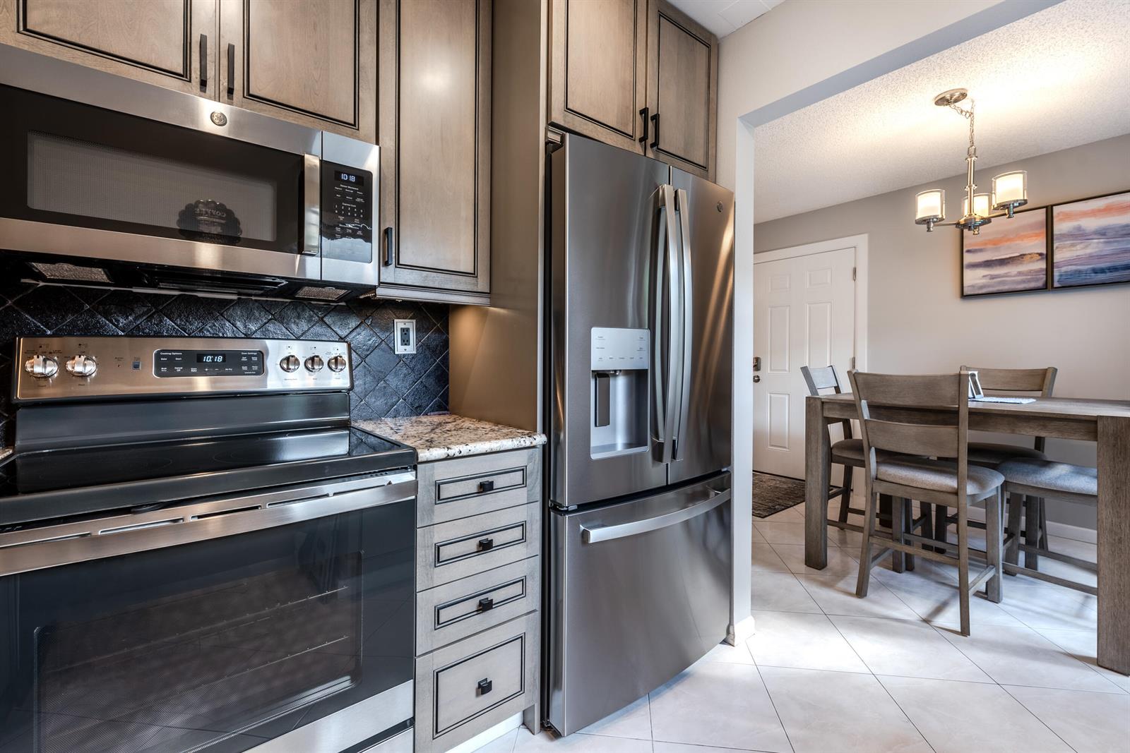 A kitchen features stainless steel appliances, dark wood cabinets, and a dining area beyond — 184 Piedmont D # D, Delray Beach FL 33484, DELRAY BEACH, FL