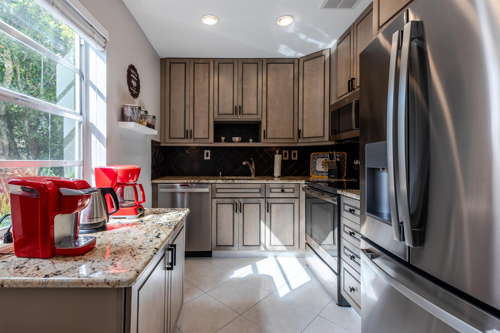 A kitchen with light wood cabinets, granite countertops, stainless steel appliances, and a red coffee maker — 184 Piedmont D # D, Delray Beach FL 33484, DELRAY BEACH, FL