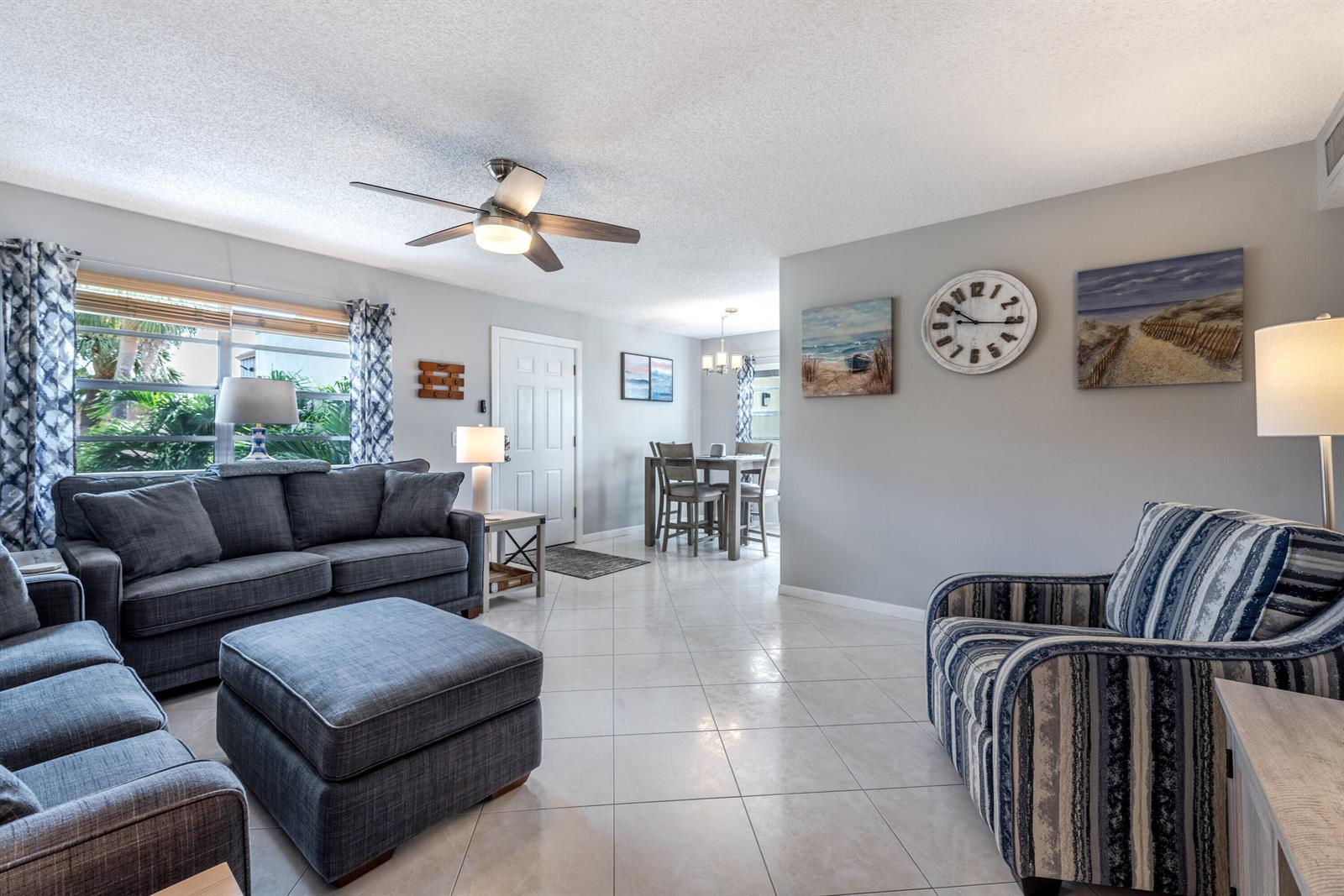 A living room features gray tile floors, a sectional sofa, a striped armchair, and wall art — 184 Piedmont D # D, Delray Beach FL 33484, DELRAY BEACH, FL