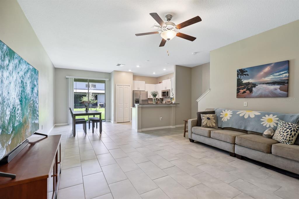 A living room with tile flooring, a ceiling fan, and an open kitchen with white cabinets — 14323 EASY GOER STREET, RUSKIN, FL