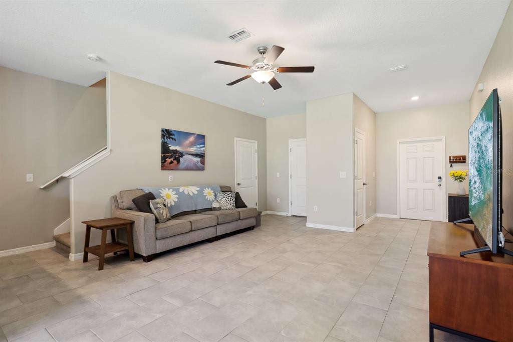 A living room features light tile flooring, a gray sofa, and a wall-mounted television — 14323 EASY GOER STREET, RUSKIN, FL