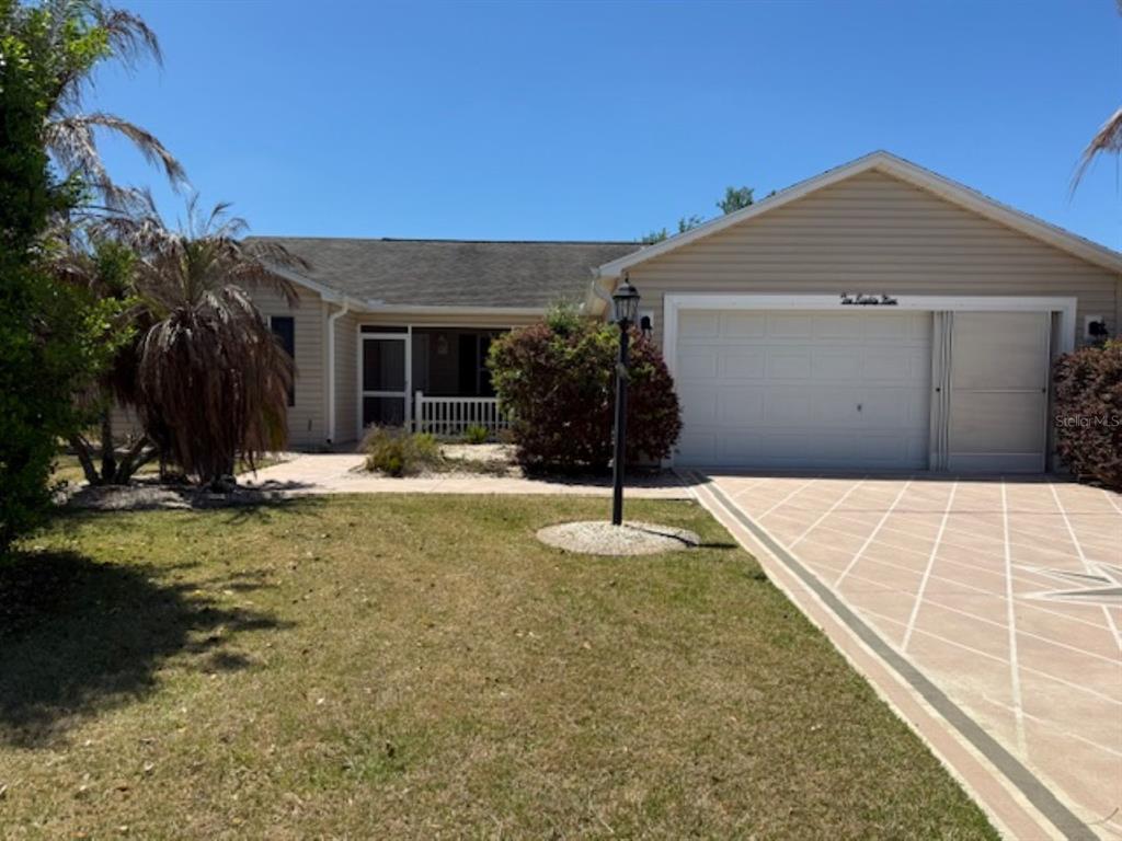 A single-story house with beige siding, a two-car garage, and a screened front porch — 1089 NASH LOOP, THE VILLAGES, FL