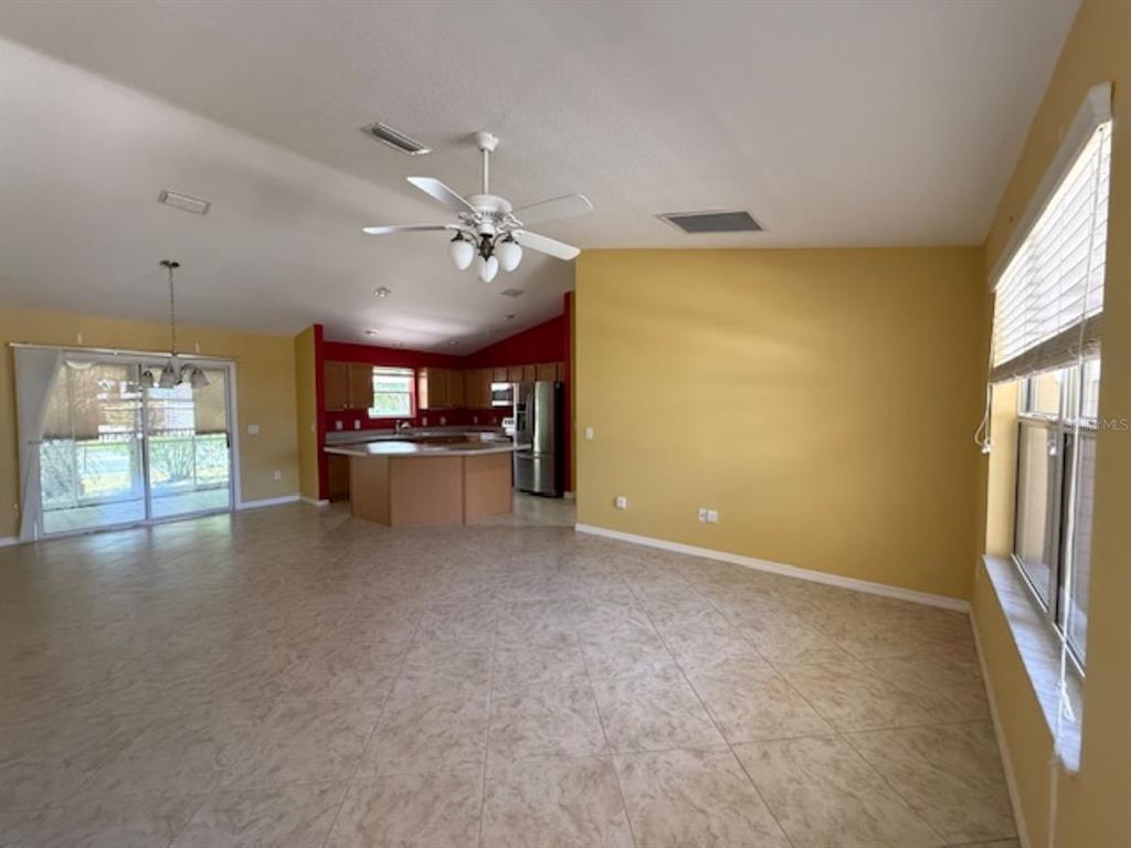 An open-concept living area with tile floors, yellow walls, a ceiling fan, and a kitchen — 1089 NASH LOOP, THE VILLAGES, FL