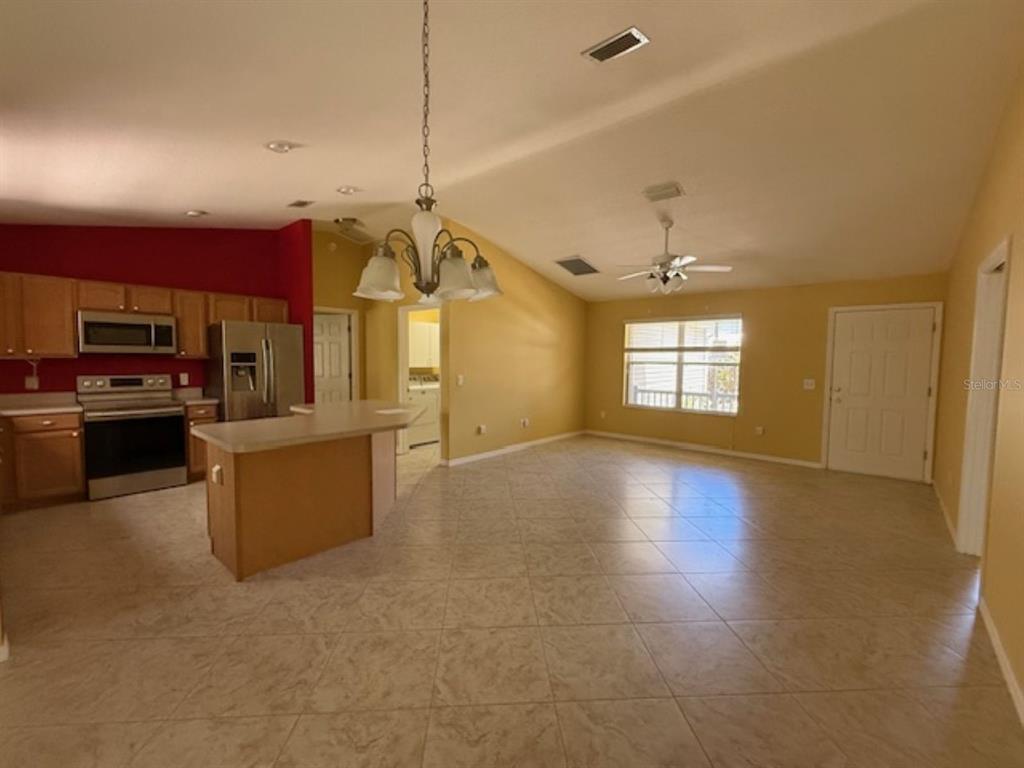 An open-concept kitchen and living area with tile flooring, light-colored walls, and vaulted ceilings — 1089 NASH LOOP, THE VILLAGES, FL