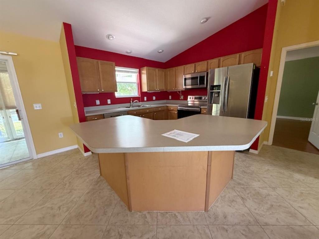 A kitchen with light wood cabinets, a large peninsula, and red accent walls — 1089 NASH LOOP, THE VILLAGES, FL