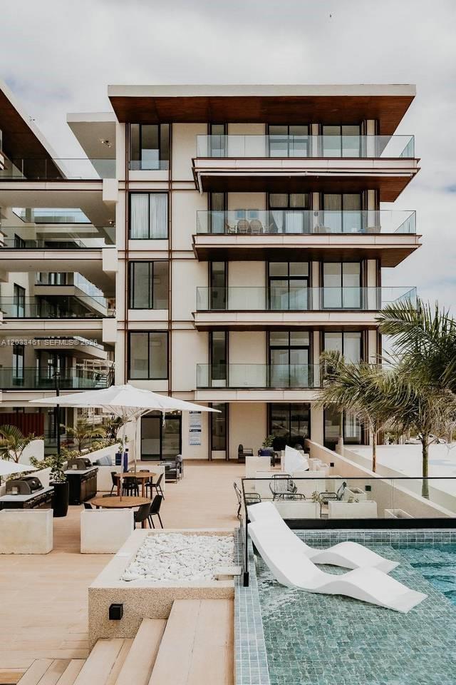 A multi-story modern building with balconies overlooks a patio area featuring a swimming pool — 1 1 # 205, FL, FL