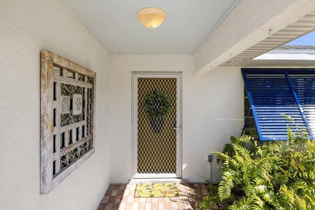 A covered front entryway features a white door with a screen, wall art, and shutters — 4731 EGRET ROAD, VENICE, FL