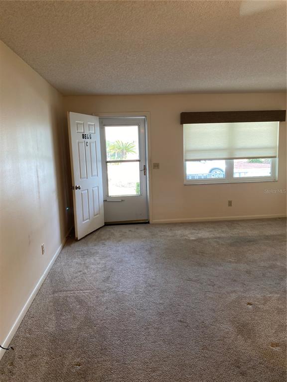 A carpeted living room features a white front door and a window with a shade — 8666 SW 92ND LANE UNIT C, OCALA, FL