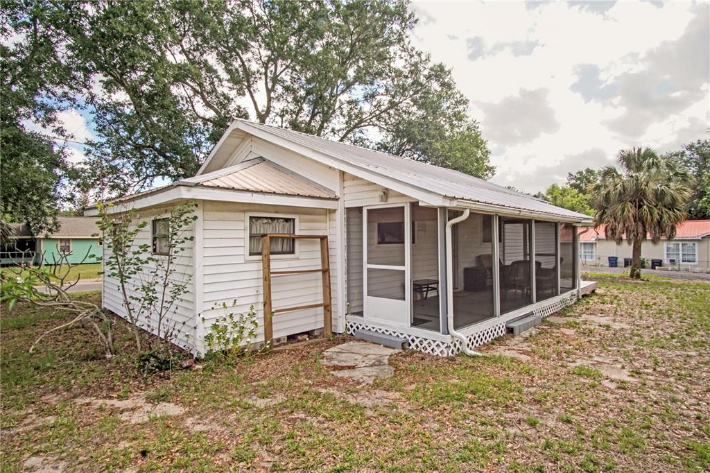 A white cottage with a metal roof and a screened-in porch sits on a grassy lot — 120 CHESNEY BOULEVARD, FROSTPROOF, FL