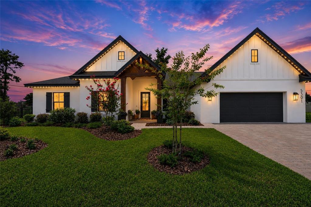 A modern farmhouse with white siding, a dark garage, and a wood-accented front entryway — 5391 CLUBHOUSE HILLS LANE, LAKELAND, FL