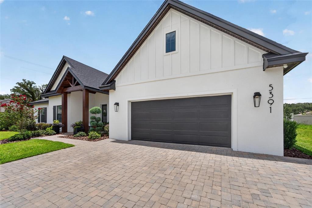 A white house with a dark garage door and a paved driveway under a blue sky — 5391 CLUBHOUSE HILLS LANE, LAKELAND, FL