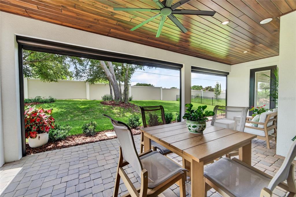 A covered patio features a wood-paneled ceiling, a ceiling fan, and a dining set — 5391 CLUBHOUSE HILLS LANE, LAKELAND, FL