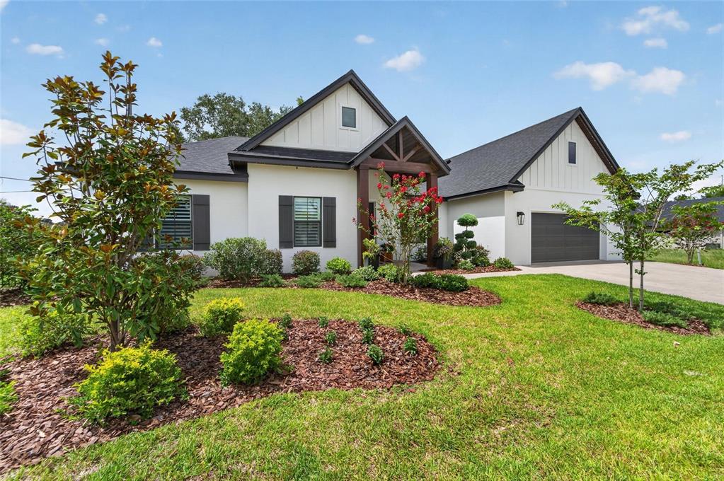 A single-story white house with a dark roof, wooden porch accents, and a two-car garage — 5391 CLUBHOUSE HILLS LANE, LAKELAND, FL