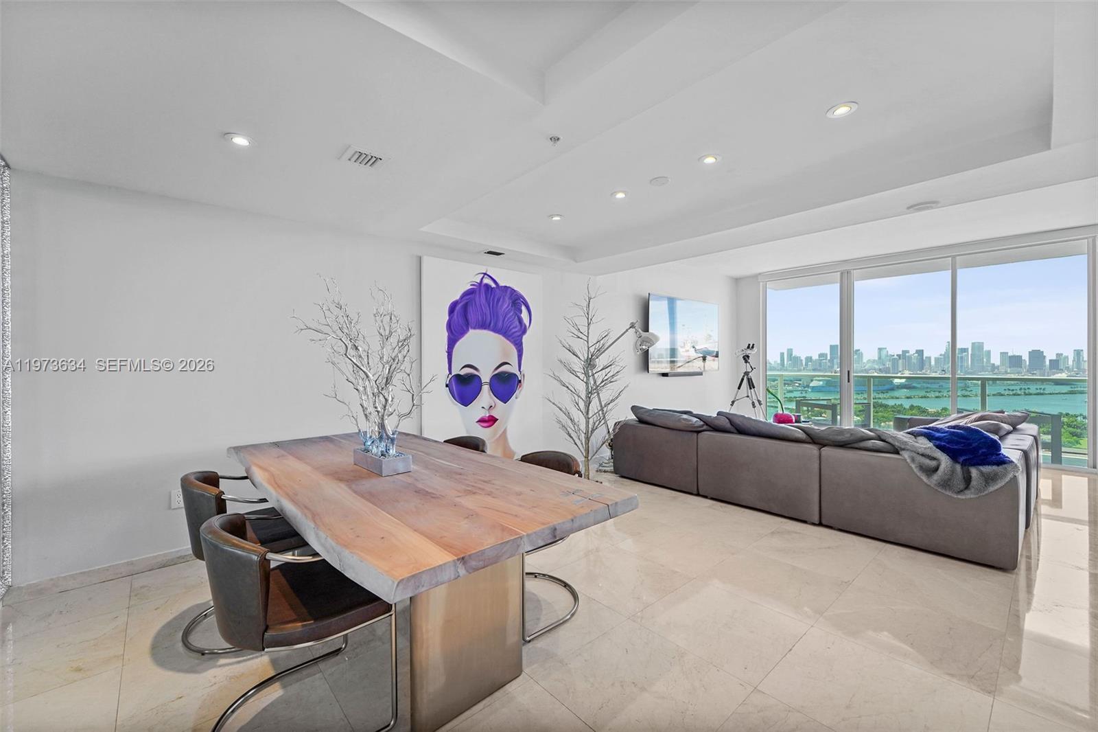 A modern living and dining area features a live-edge table, large portrait, and city views — 650 West Ave, Miami Beach FL 33139, MIAMI BEACH, FL