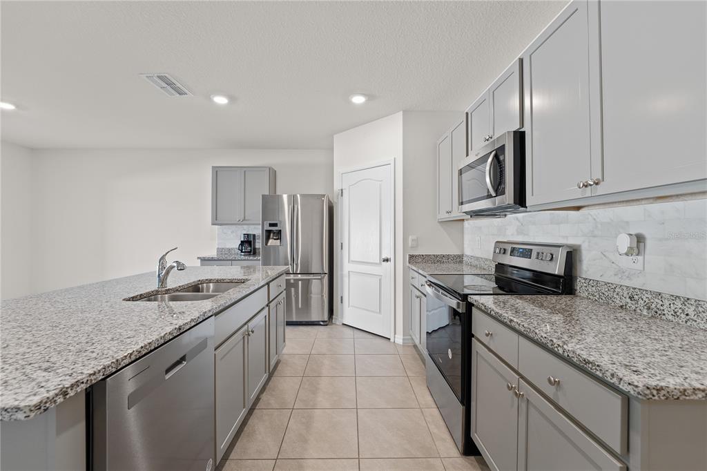 A modern kitchen features gray cabinets, granite countertops, stainless steel appliances, and a central island — 571 TANARO LANE, HAINES CITY, FL