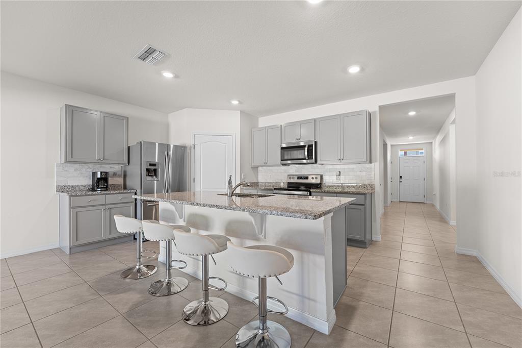 A kitchen with gray cabinets, granite countertops, a center island with bar stools, and tile flooring — 571 TANARO LANE, HAINES CITY, FL