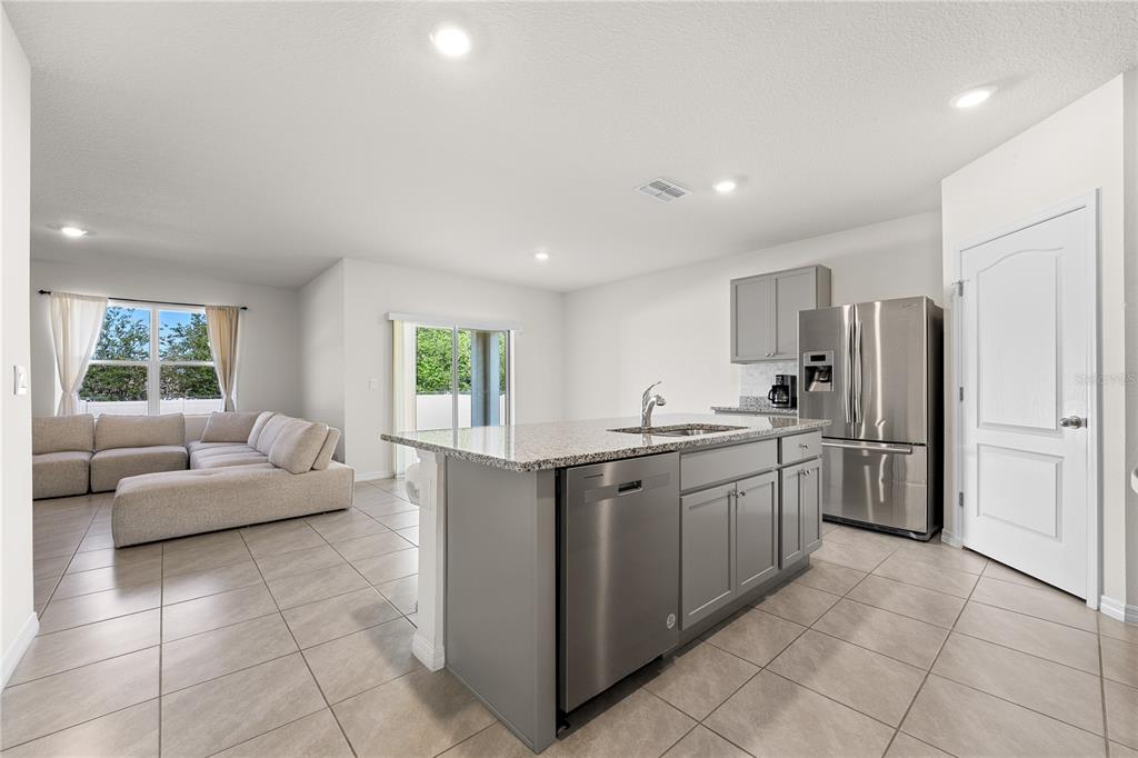 An open-concept kitchen with a gray island and stainless steel appliances overlooks a living area — 571 TANARO LANE, HAINES CITY, FL
