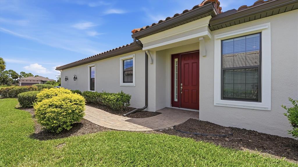 A beige house exterior features a red front door, a brick walkway, and landscaping — 10103 SAINT FRANCIS TERRACE, PALMETTO, FL