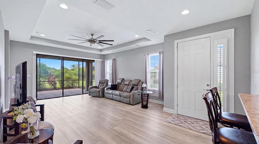 A living room with light wood-look flooring, gray walls, a tray ceiling, and sliding glass doors — 10103 SAINT FRANCIS TERRACE, PALMETTO, FL