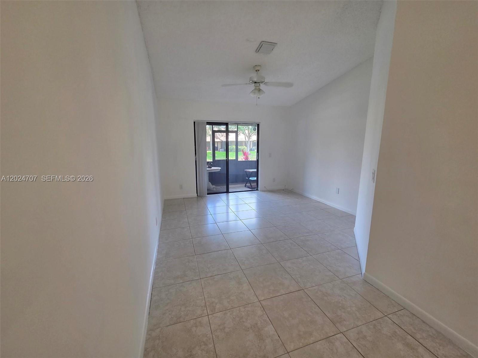 An empty living room features white walls, light tile flooring, and a sliding glass door — 3686 NW 83rd Ln # 3686, Sunrise FL 33351, SUNRISE, FL