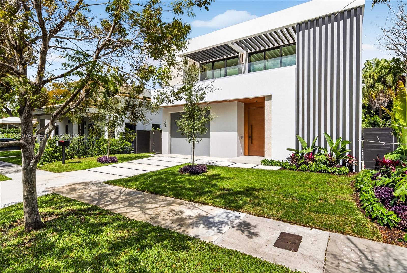 A modern two-story house features a gray garage door, a wooden front door, and a balcony — 609 SW 24th Rd, Miami FL 33129, MIAMI, FL