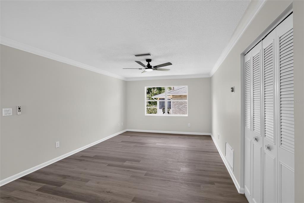 An empty room features gray wood-look flooring, light gray walls, a ceiling fan, and louvered closet doors — 1289 WORTHINGTON DRIVE, DELTONA, FL