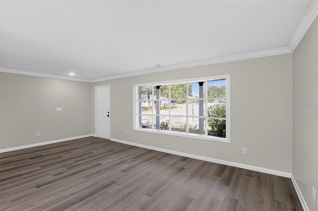 An empty room with gray walls, wood-look flooring, a white door, and a large window — 1289 WORTHINGTON DRIVE, DELTONA, FL