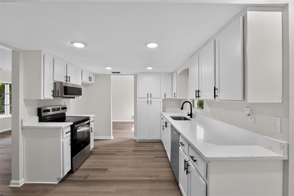 A modern kitchen features white cabinets, quartz countertops, stainless steel appliances, and wood-look flooring — 1289 WORTHINGTON DRIVE, DELTONA, FL