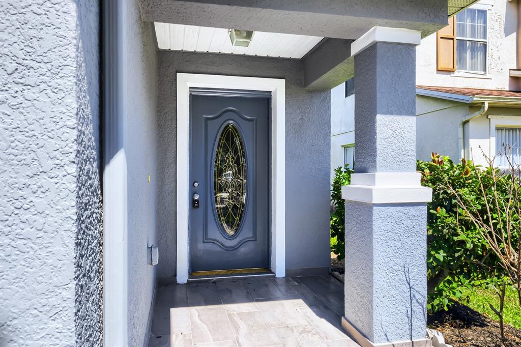 A gray front door with an oval glass insert sits under a covered porch entryway — 2858 PAYNES PRAIRIE CIRCLE, KISSIMMEE, FL