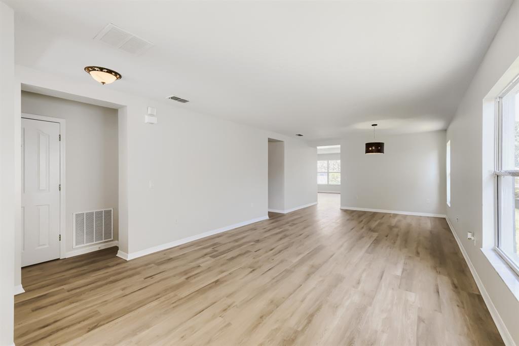 An empty living room features light wood-look flooring, white walls, and a dark pendant light — 2858 PAYNES PRAIRIE CIRCLE, KISSIMMEE, FL