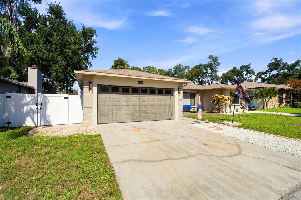 A single-story house with a beige exterior, a two-car garage, and a white privacy fence — 1830 WILLOW OAK DRIVE W, PALM HARBOR, FL