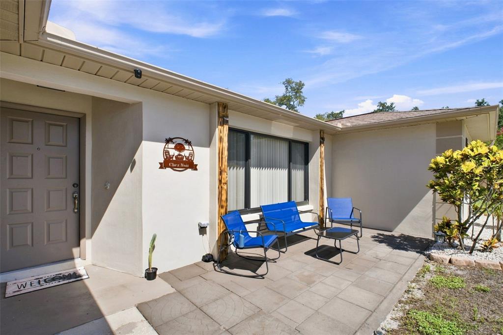 A patio with blue chairs and a small table sits outside a house entrance — 1830 WILLOW OAK DRIVE W, PALM HARBOR, FL
