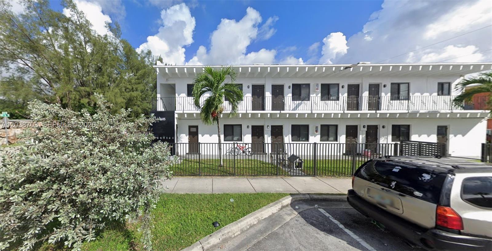 A two-story white apartment building with a black metal fence and a parked car — FLORIDA CITY, FL