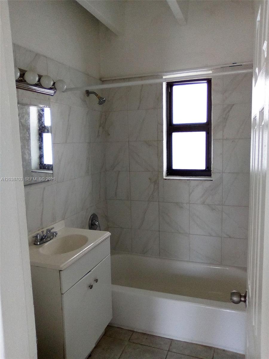 A bathroom features a white vanity, a tiled shower-tub combination, and a window — FLORIDA CITY, FL