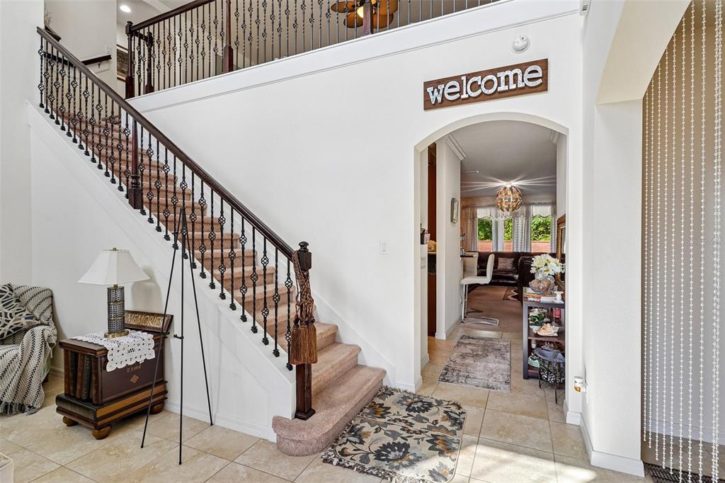 A foyer features a carpeted staircase with dark wood railings and an arched entryway — 17407 BELLA NOVA DRIVE, ORLANDO, FL