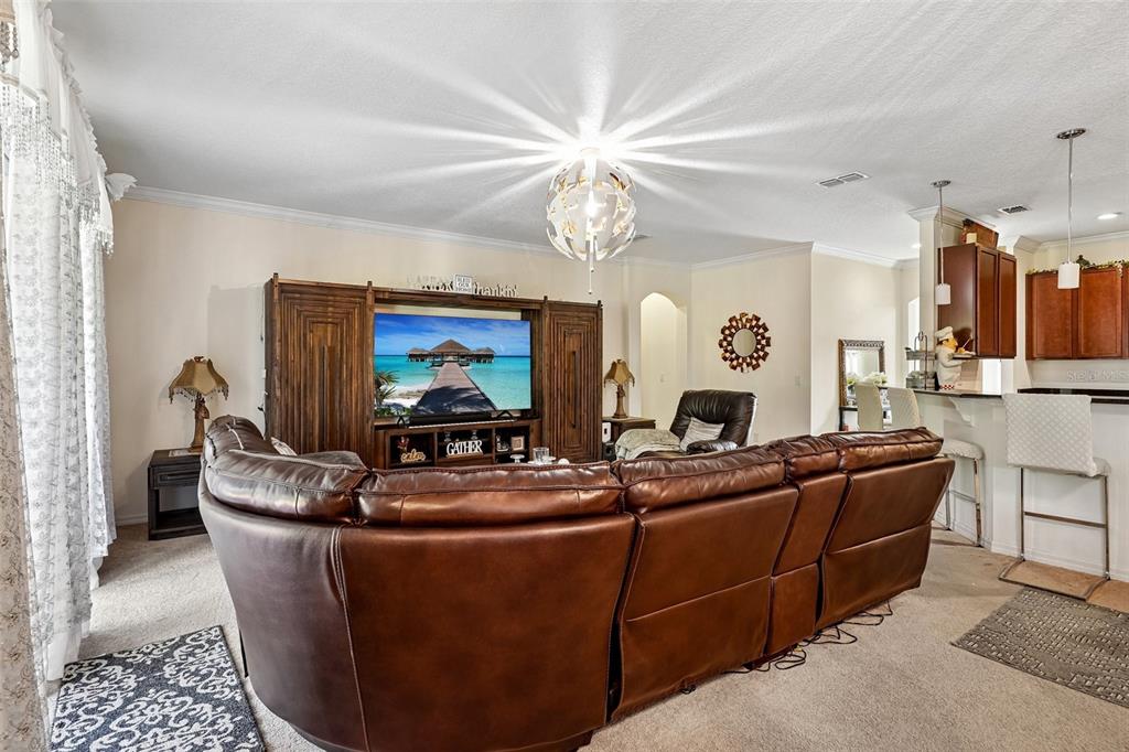 A living room features a large brown leather sectional, a wooden entertainment center, and kitchen — 17407 BELLA NOVA DRIVE, ORLANDO, FL