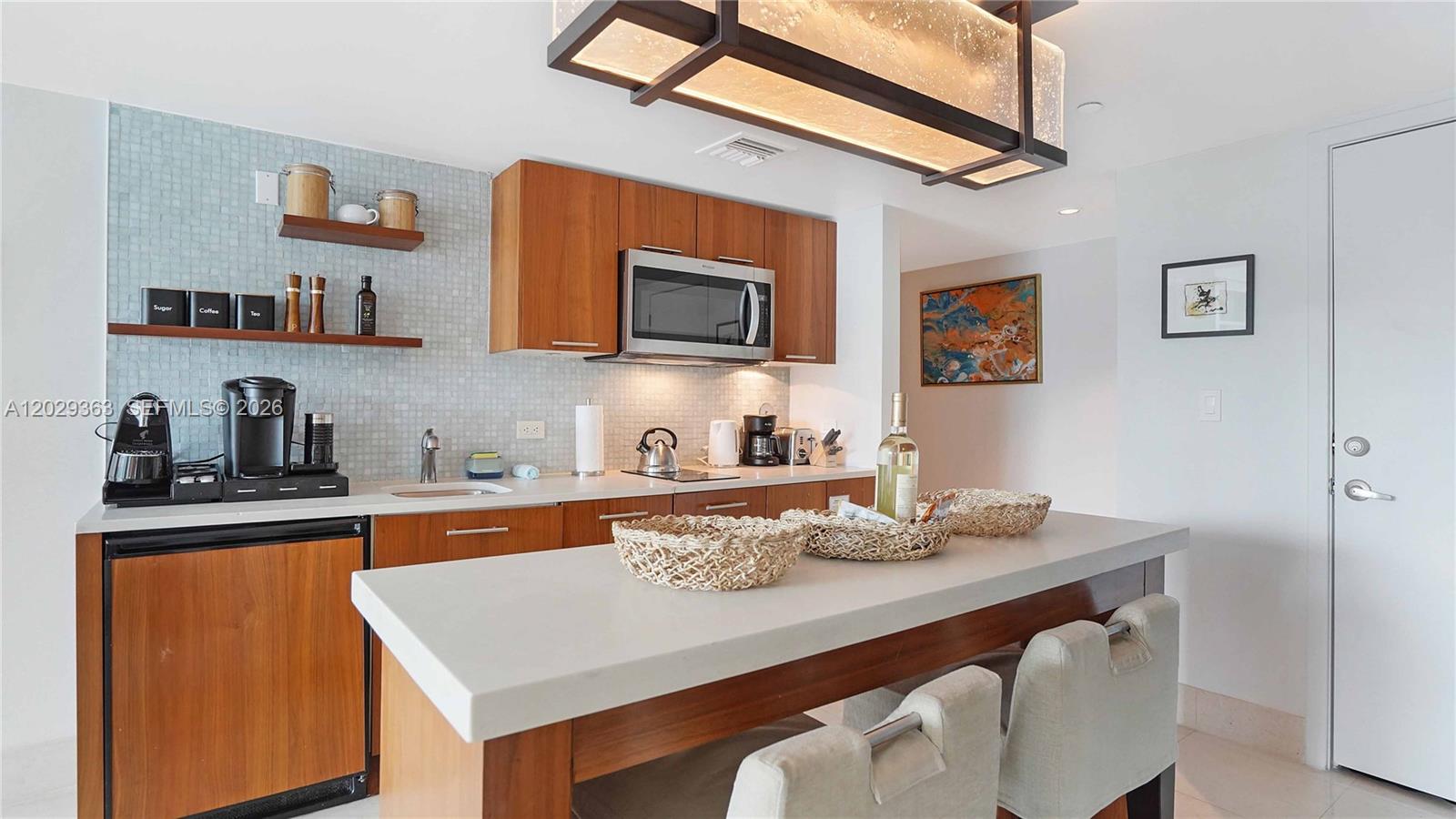 A kitchen features wood cabinets, a light-colored countertop, and a central island with stools — 6801 Collins Ave # 315, Miami Beach FL 33141, MIAMI BEACH, FL